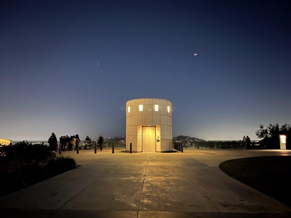 洛杉磯格里斐斯天文台（Griffith Observatory）夜晚景觀，簡約幾何結構的觀測塔在深藍夜色下發出柔和黃光，俯瞰城鎮燈火。