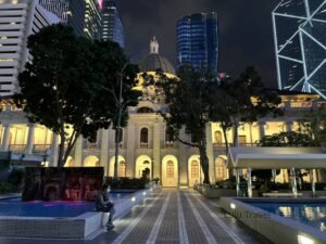夜晚燈光下的歷史建築與現代高樓並列，前方廣場有人靜坐，展現城市中舊與新的對比景色