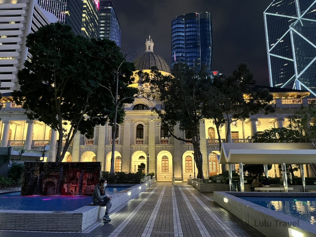 Hong Kong Trip Beyond the Surface: A Strategic 4-Day Itinerary 夜晚燈光下的歷史建築與現代高樓並列,前方廣場有人靜坐,展現城市中舊與新的對比景色