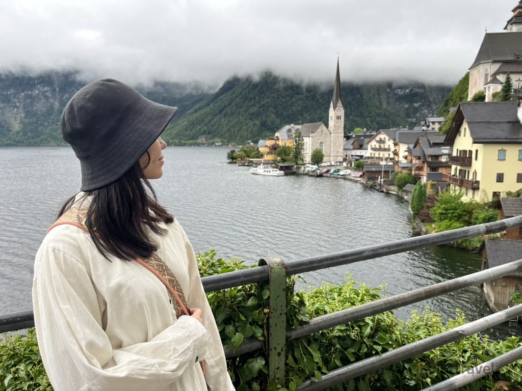 歐洲旅遊 一名女子站在歐洲古城堡的石牆階梯旁,戴著黑色帽子眺望城市景色,背景為奧地利薩爾茲堡老城區與陰雲密布的天空,展現旅行中的靜謐與歷史氛圍