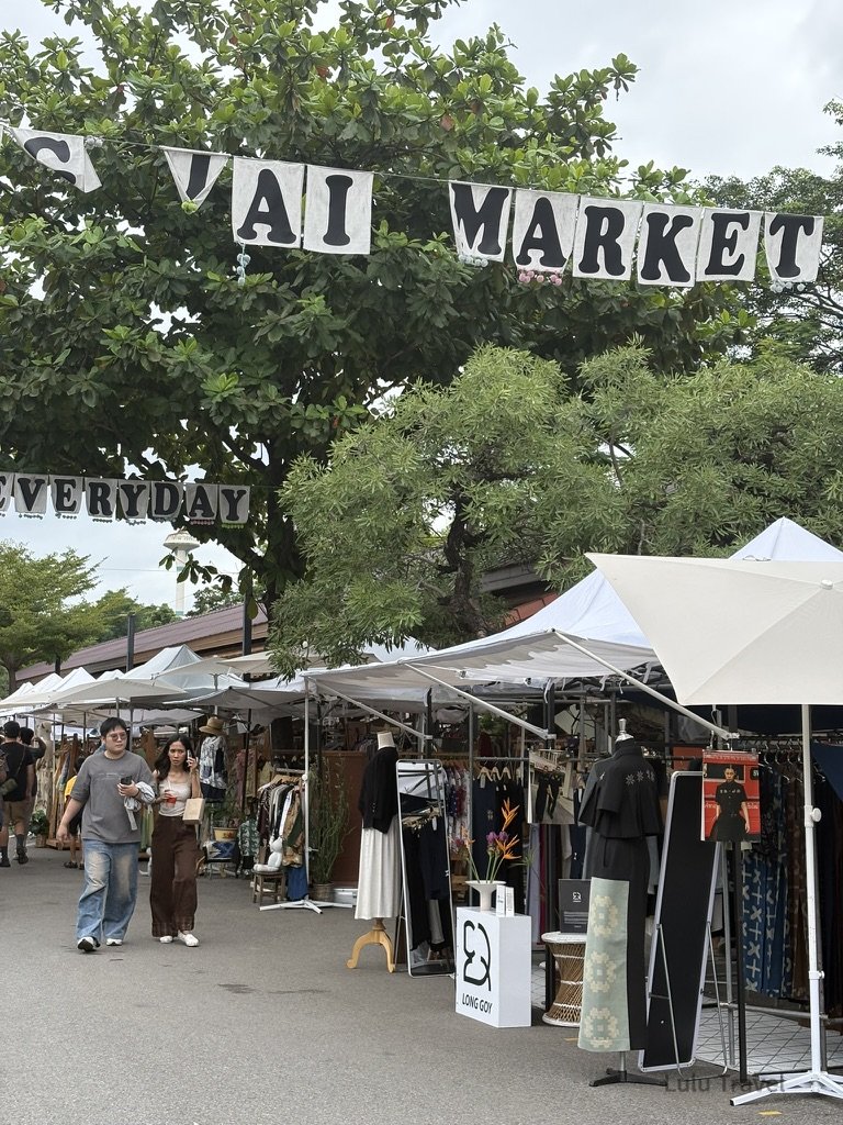 泰國曼谷 JJ Market 市集街景，戶外帳篷攤位販售服飾與設計商品，旅人漫步其中，呈現充滿生活感的曼谷文青市集氛圍
