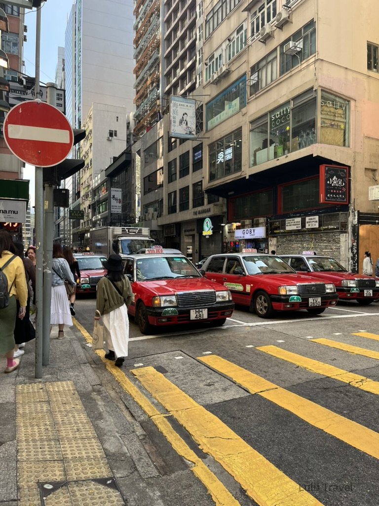 Hong Kong Trip Beyond the Surface: A Strategic 4-Day Itinerary 香港中環街景,紅色計程車行駛在狹窄街道上,兩側為高密度商業大樓與行人交錯的城市畫面