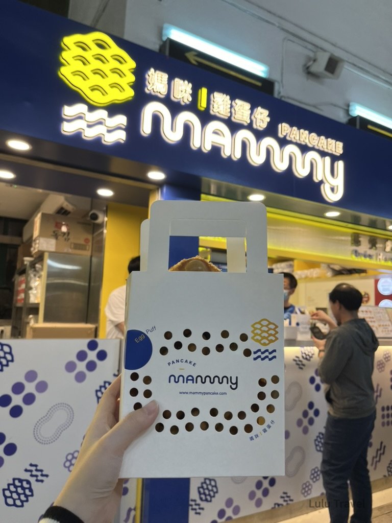 Hong Kong Trip Beyond the Surface: A Strategic 4-Day Itinerary 香港街頭 Mammy Pancake 雞蛋仔店,旅人手持外帶包裝站在店前,體驗香港經典街頭小吃