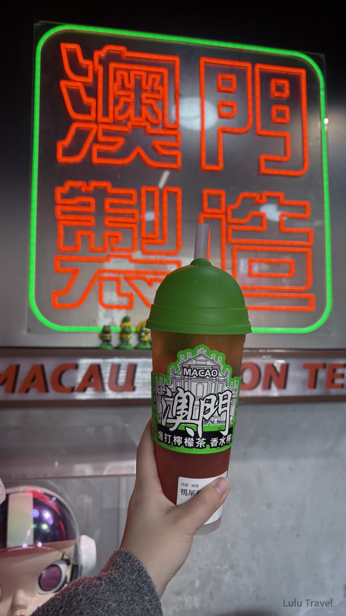 10+ Must-Eat Stalls in Macau: A No-Backtrack Food Route for 2 Days 1 Night 澳門街頭夜景,一杯澳門關前正宗凍檸茶前景,背景為紅色霓虹招牌,呈現澳門老城區夜晚的港式街頭氛圍與在地飲食文化