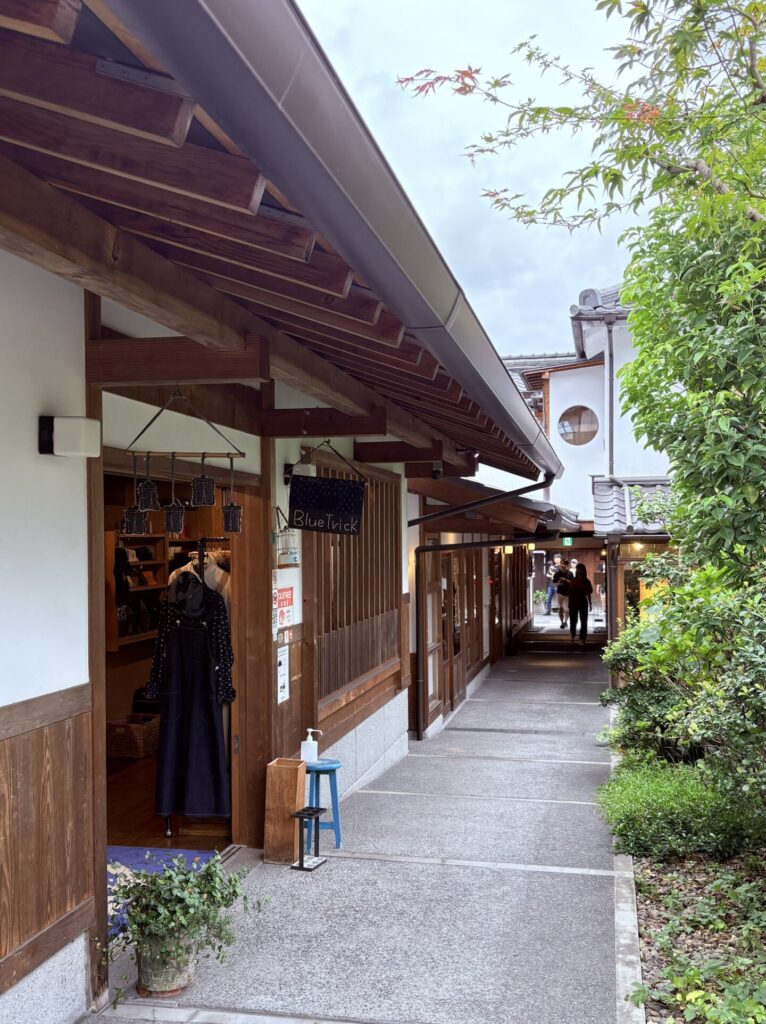 日本岡山倉敷美觀地區，傳統町屋改建的商店街巷道，木造建築與綠意交錯，遊客沿著步道散步