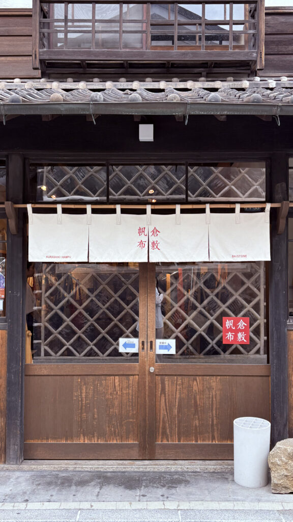 日本岡山倉敷美觀地區的傳統町屋店家外觀，木造建築搭配白色門簾與格子拉門，呈現江戶風格的歷史街景