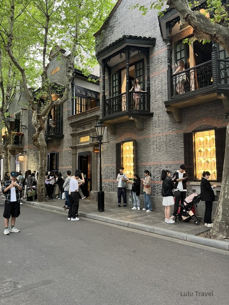 Shanghai City Walk — What I Got Wrong and What I'd Do Differently 上海街頭林蔭大道旁的歷史建築外觀,灰磚洋樓立面與陽台設計,行人聚集拍照與排隊,呈現上海租界風格街景