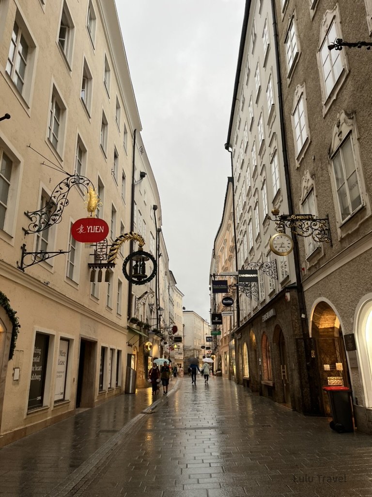 Traveling Europe with Elderly Family — Planning Logic and Honest Reflections 奧地利薩爾斯堡老城街道,雨後石板路與歷史招牌,行人漫步其間