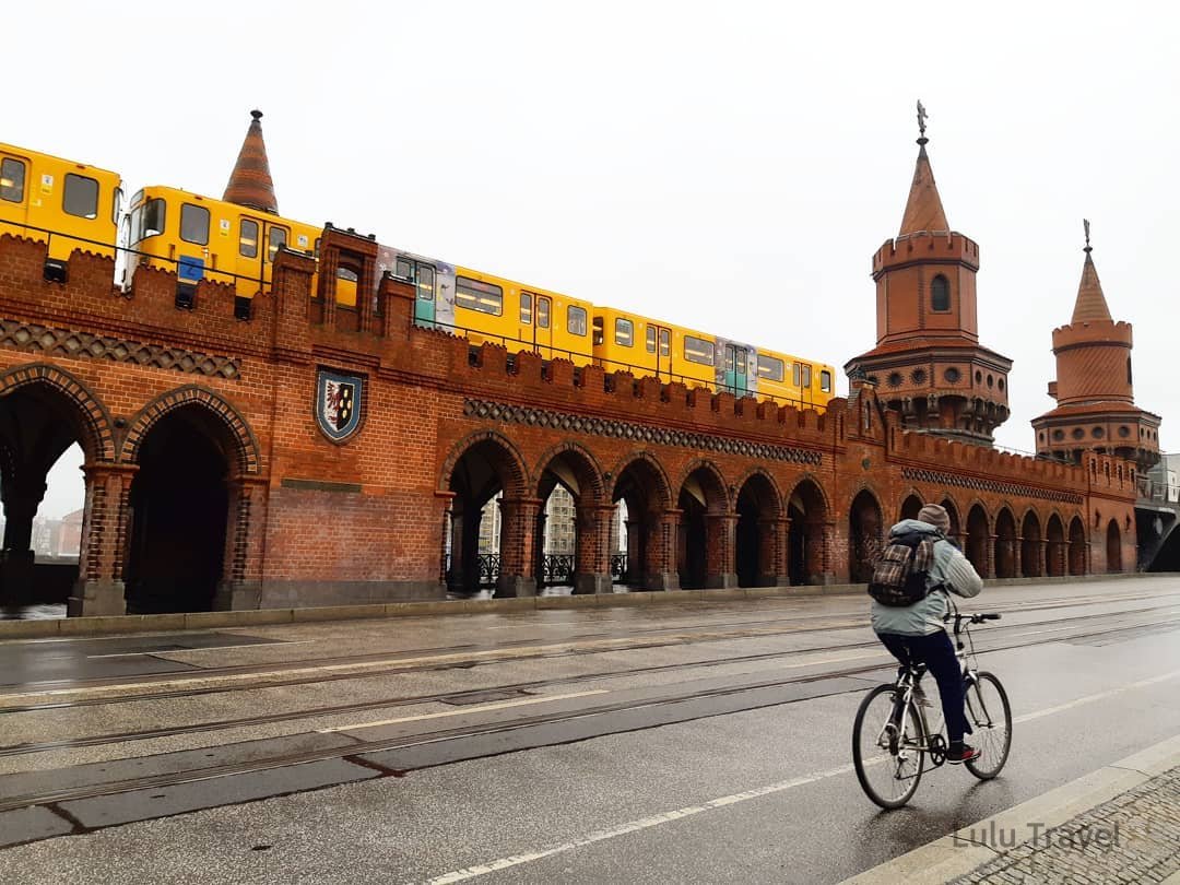 柏林標誌性的奧伯鮑姆橋（Oberbaum Bridge）紅色磚造雙塔建築，黃色的柏林地鐵（U-Bahn）列車正行經橋面。