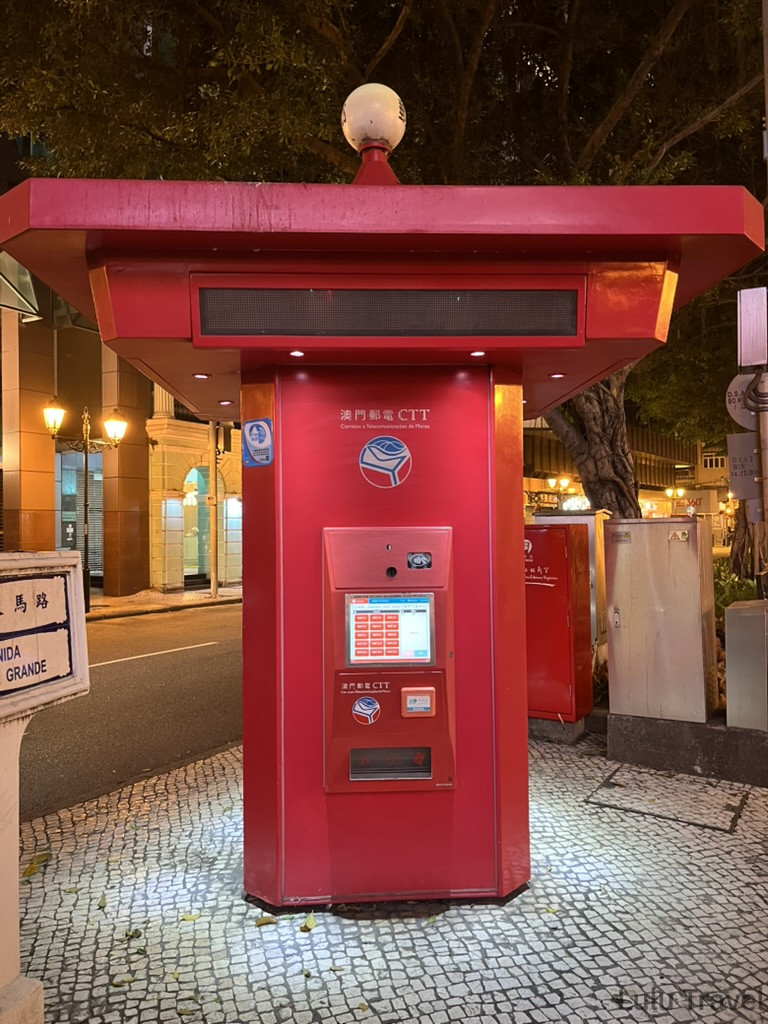 Accidental Macau Travel: A Spontaneous 2-Day Macau Self-Guided Itinerary 澳門議事亭前地附近的紅色澳門郵電 CTT 自助郵筒亭,夜晚燈光照亮鵝卵石地面