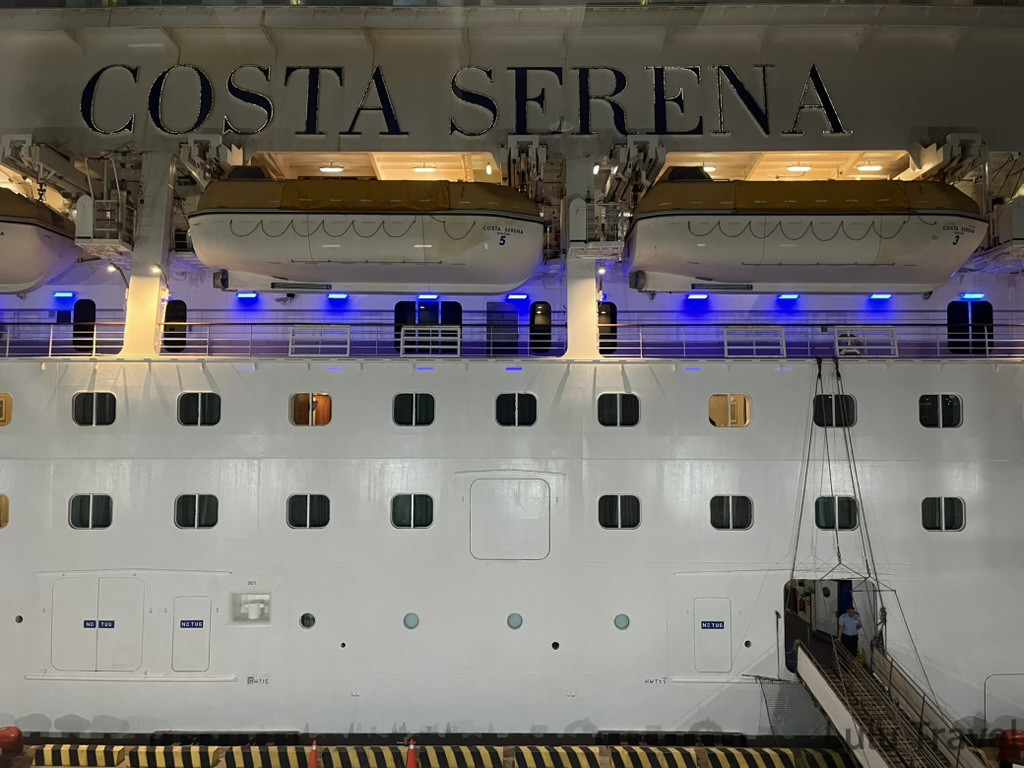 夜晚停泊在港口的歌詩達莎倫娜號（Costa Serena）郵輪外觀，巨大船身上掛著救生艇與連接著的登船空橋，展現這座海上移動城堡的真實比例與震撼感。