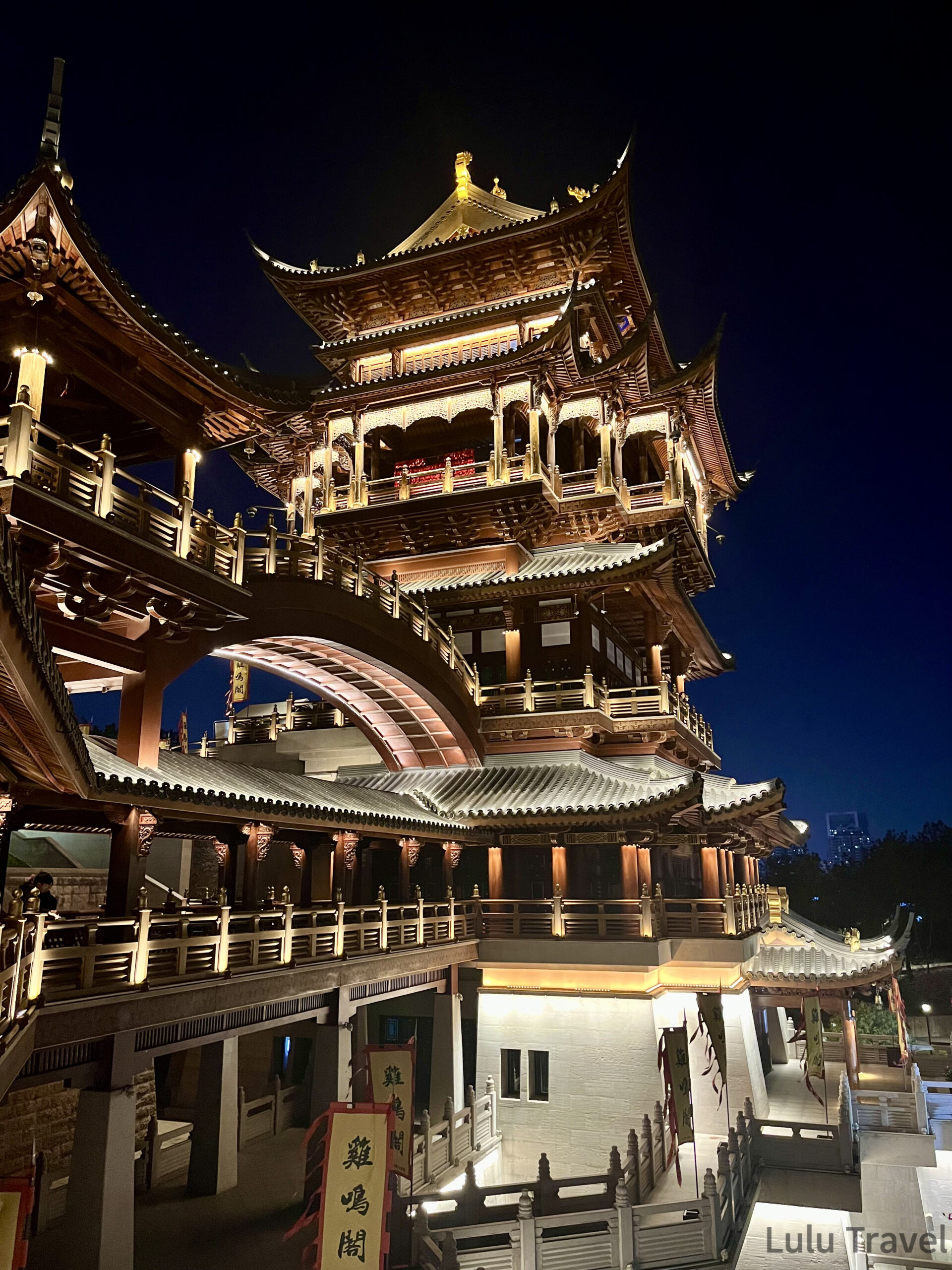 中國出差|深圳的震撼反差與義烏意外挖到的免費景點 義烏雞鳴閣多層樓閣夜景全貌,傳統木雕飛簷層層疊起,暖黃燈光打亮整座建築,前景可見雞鳴閣招牌旗幟