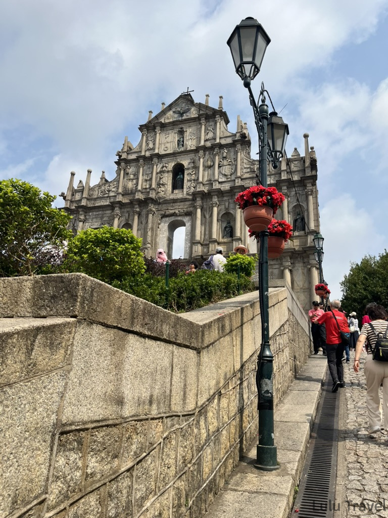 Accidental Macau Travel: A Spontaneous 2-Day Macau Self-Guided Itinerary 從澳門大三巴側邊石牆角度拍攝,前景為路燈掛著紅色花籃,背景為巴洛克立面