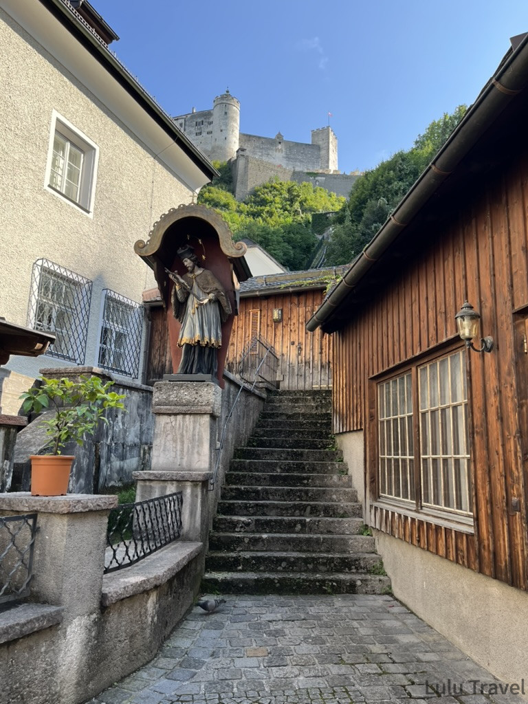 Salzburg Travel Guide — 5 Highlights and Why It's More Than a Mozart Stopover 薩爾斯堡老城石階小巷,牆上嵌有聖人雕像神龕,仰望可見霍亨薩爾斯堡城堡矗立山頂