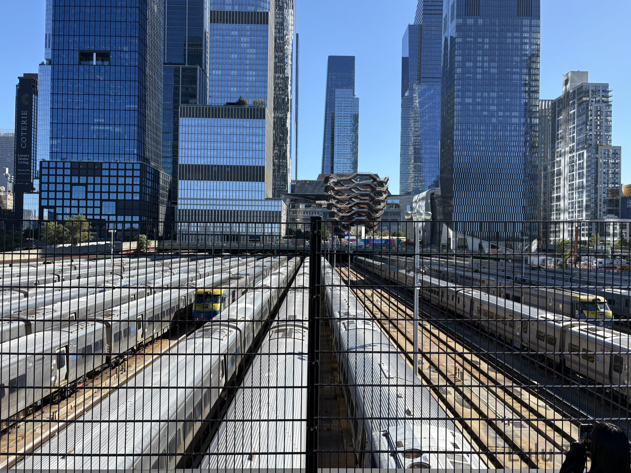 紐約行程規劃|DUMBO、百老匯、布魯克林到波士頓一日遊 紐約 Hudson Yards 景觀實拍,從高處俯瞰密集的 LIRR 鐵道與停靠的銀色列車,背景為著名的蜂巢狀建築 The Vessel 與曼哈頓現代摩天大樓群,展現極致的都市工業尺度。