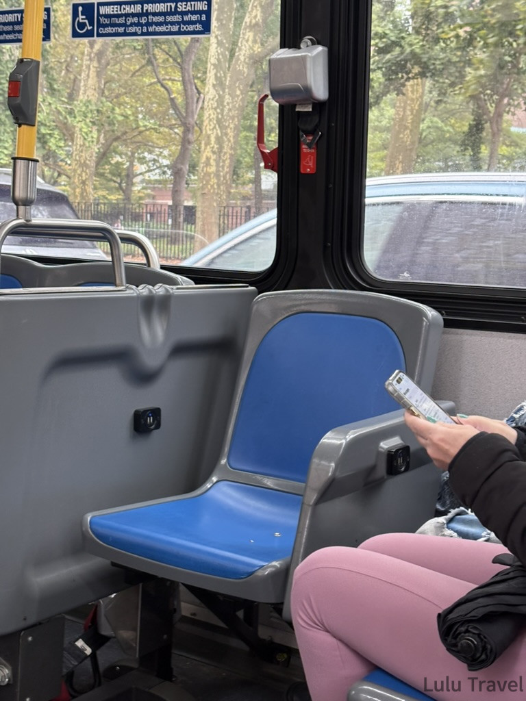 紐約自由行 | 旅費明細、交通技巧與住宿避雷全記錄 紐約公車內部實拍,展示了妳提到的拉繩式下車鈴細節,藍色塑膠座椅旁可見乘客正在使用手機,光線充足且富有生活感。