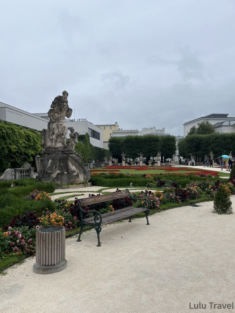 Salzburg Travel Guide — 5 Highlights and Why It's More Than a Mozart Stopover 薩爾斯堡米拉貝爾宮花園陰雨天景色,幾何對稱花圃盛開紅色花卉,遠景可見霍亨薩爾斯堡城堡