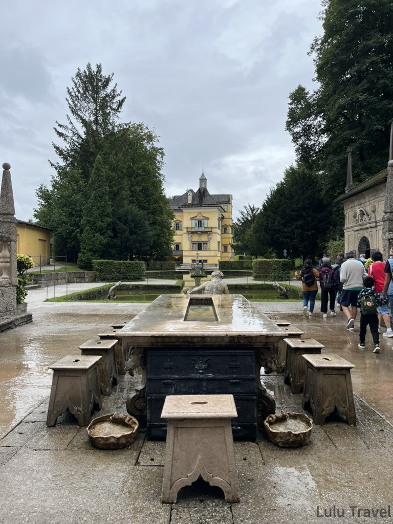 Salzburg Travel Guide — 5 Highlights and Why It's More Than a Mozart Stopover 薩爾斯堡海爾布倫宮 Hellbrunn 水花園,前景為石桌噴水機關,背景為黃色巴洛克宮殿建築