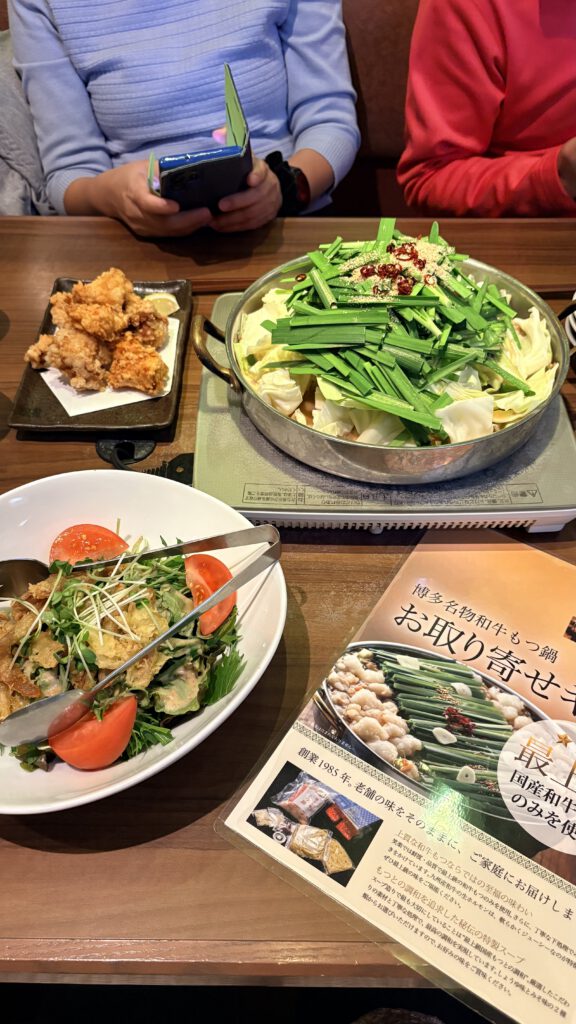 福岡自由行|日本黃金週的6 天 5 夜行程與消費明細 笑樂牛腸鍋的餐點實拍,桌上的爐子擺著鋪滿韭菜與高麗菜的牛腸鍋,旁邊有日式唐揚炸雞、沙拉以及菜單