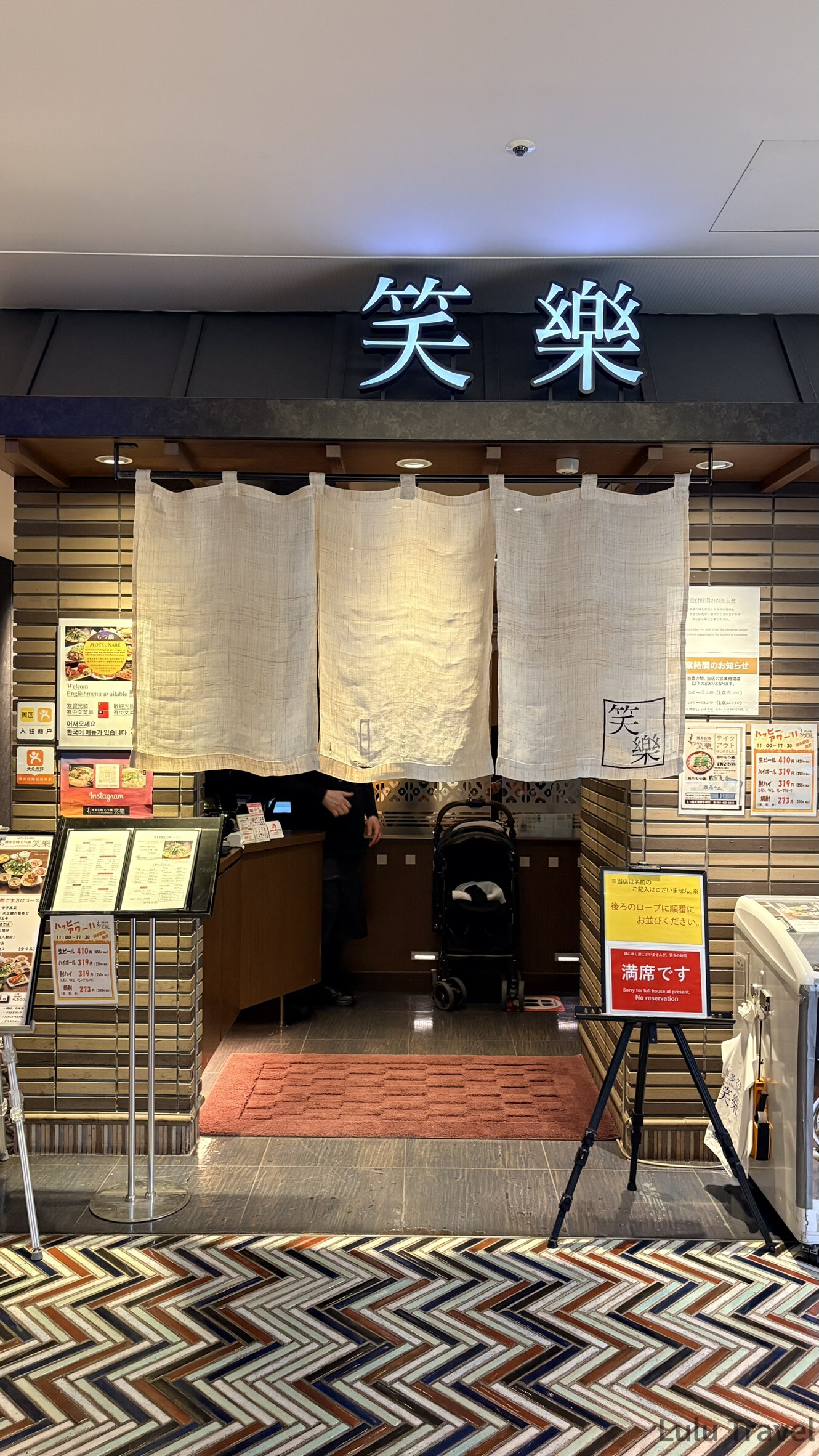 福岡自由行|日本黃金週的6 天 5 夜行程與消費明細 博多車站笑樂牛腸鍋(もつ鍋 笑樂)的店面外觀,掛著寫有店名的麻布暖簾,門口放著滿席的告示牌