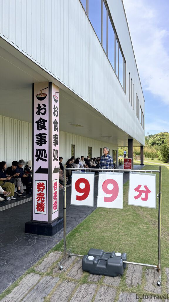 福岡自由行|日本黃金週的6 天 5 夜行程與消費明細 一蘭之森戶外廣場的等候指示牌,標示著需要等待 99 分鐘以上,後方可見排隊的人潮