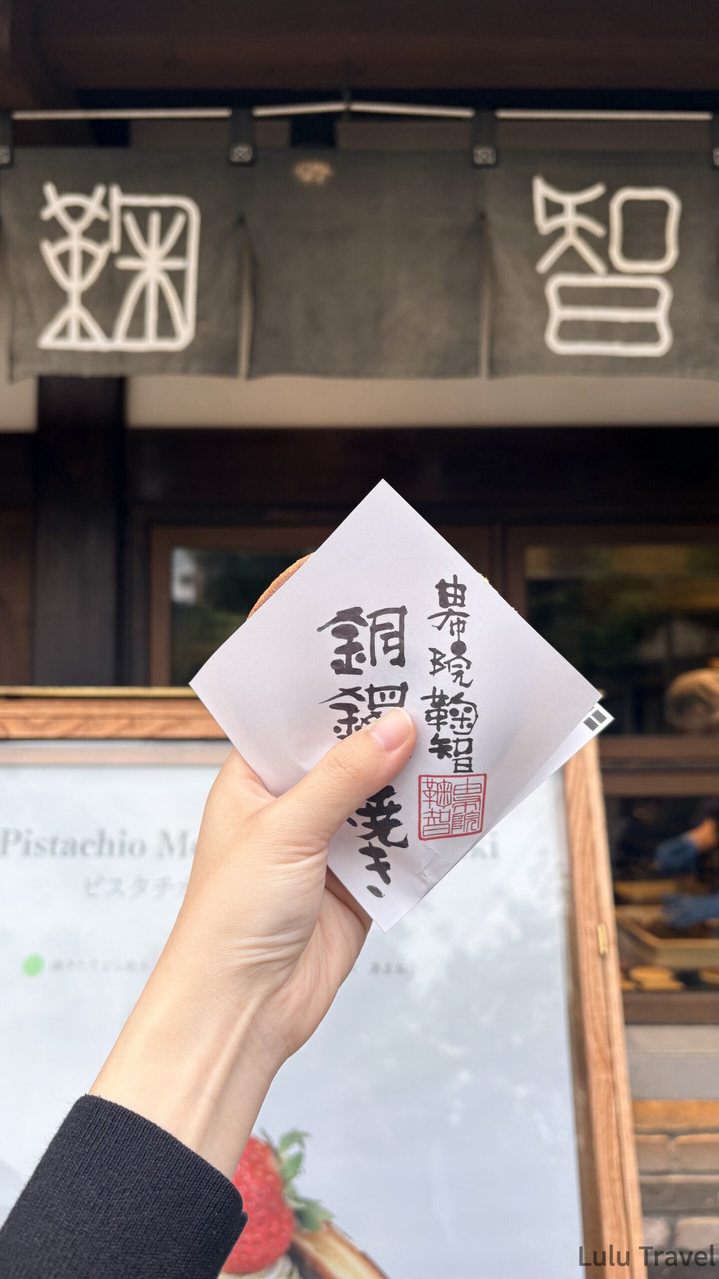 由布院兩天一夜|避開黃金週人潮的溫泉住宿與由布院之森 手持 CUCUCHI 鞠智的銅鑼燒紙袋,背景是店門口的深色暖簾