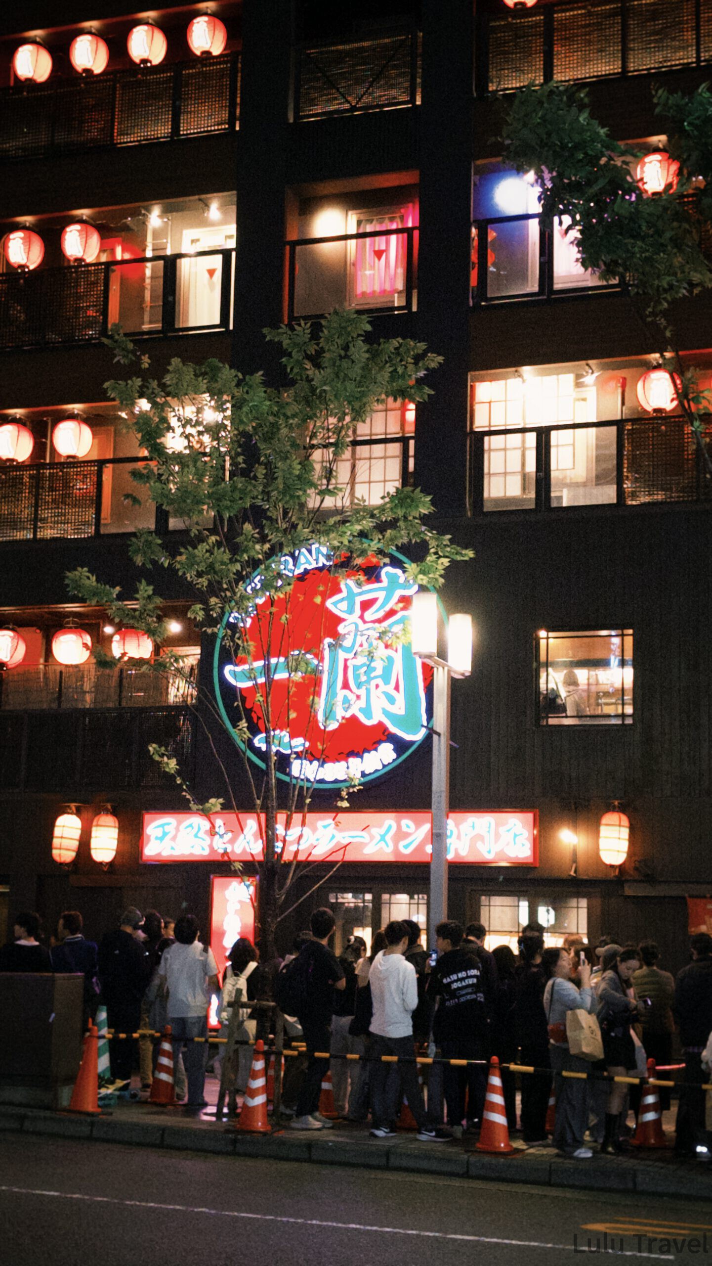 福岡自由行|日本黃金週的6 天 5 夜行程與消費明細 夜晚的一蘭拉麵總本店外觀,掛滿紅燈籠與霓虹招牌,對街聚集等看和樂團表演的人潮